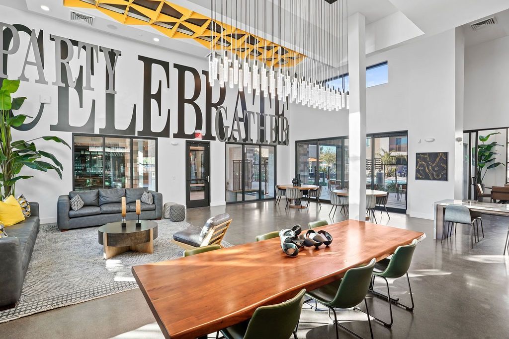 Open-concept community lounge with a long wooden table, sofas, and pendant lights.