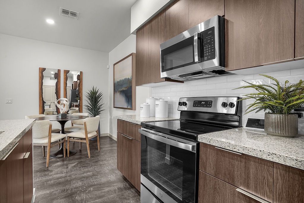 Modern kitchen with stainless steel oven and microwave, granite countertops, dark wood cabinets, and a small dining area.