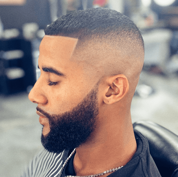 A man with a beard is getting his hair cut at a barber shop.