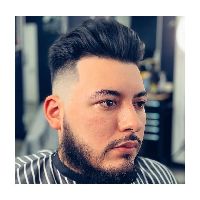 A man with a beard is getting his hair cut at a barber shop.