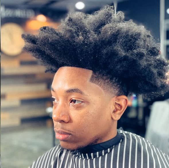 A man with a big afro is getting his hair cut at a barber shop.