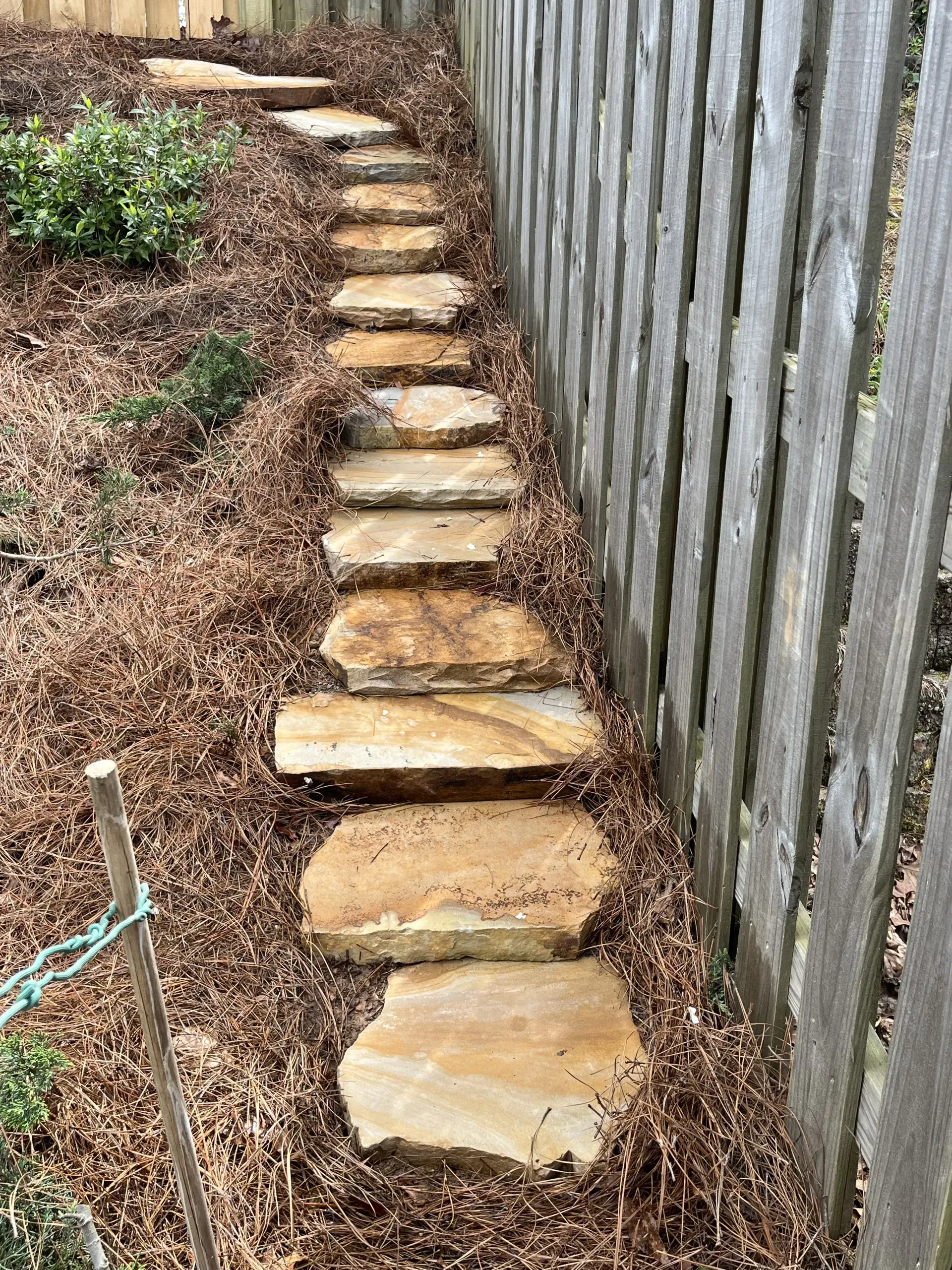 Stepping-stone path in a sloped backyard beside a wooden fence and mulch bed
