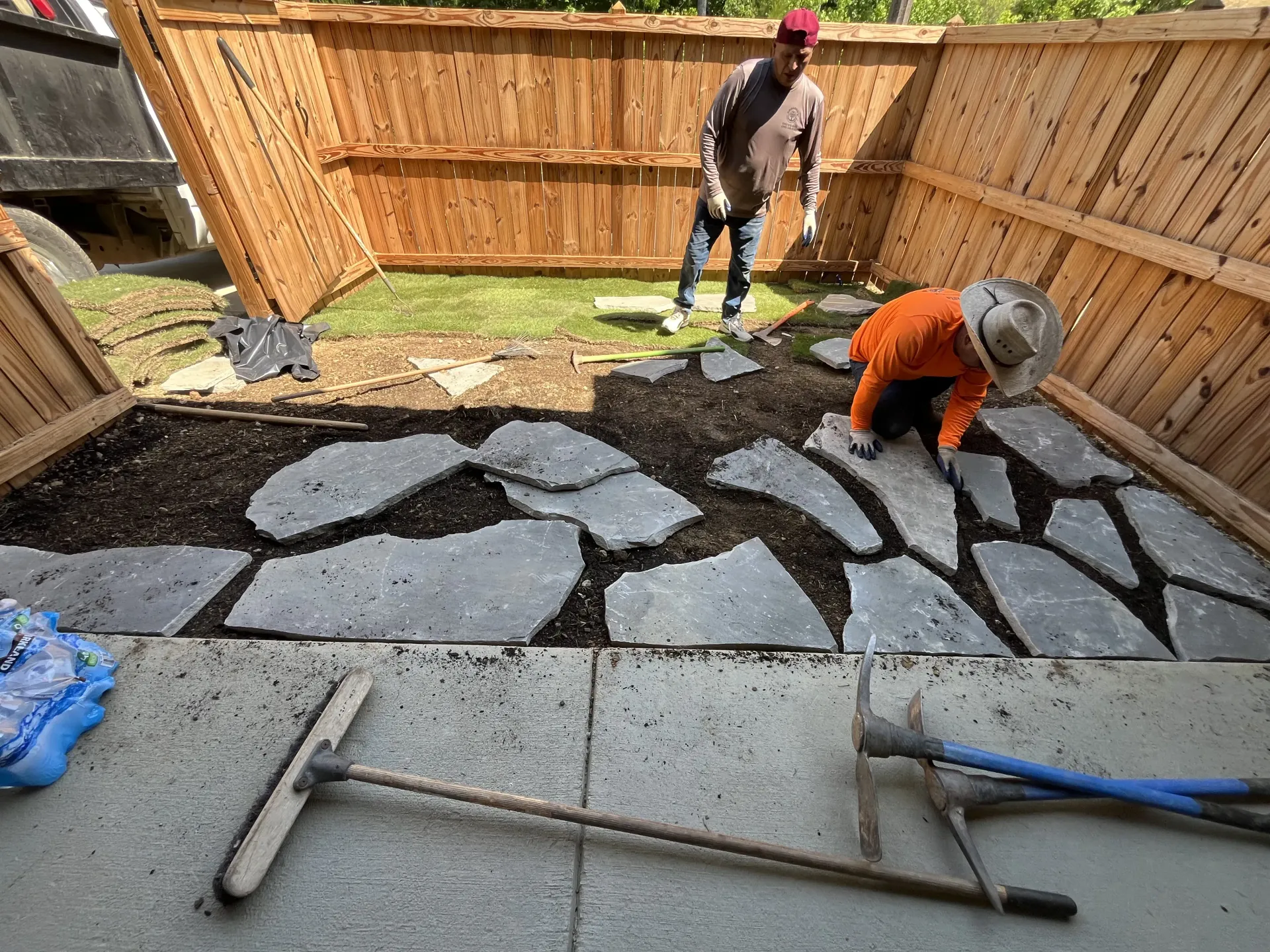 Workers laying stone pavers in a backyard patio under construction