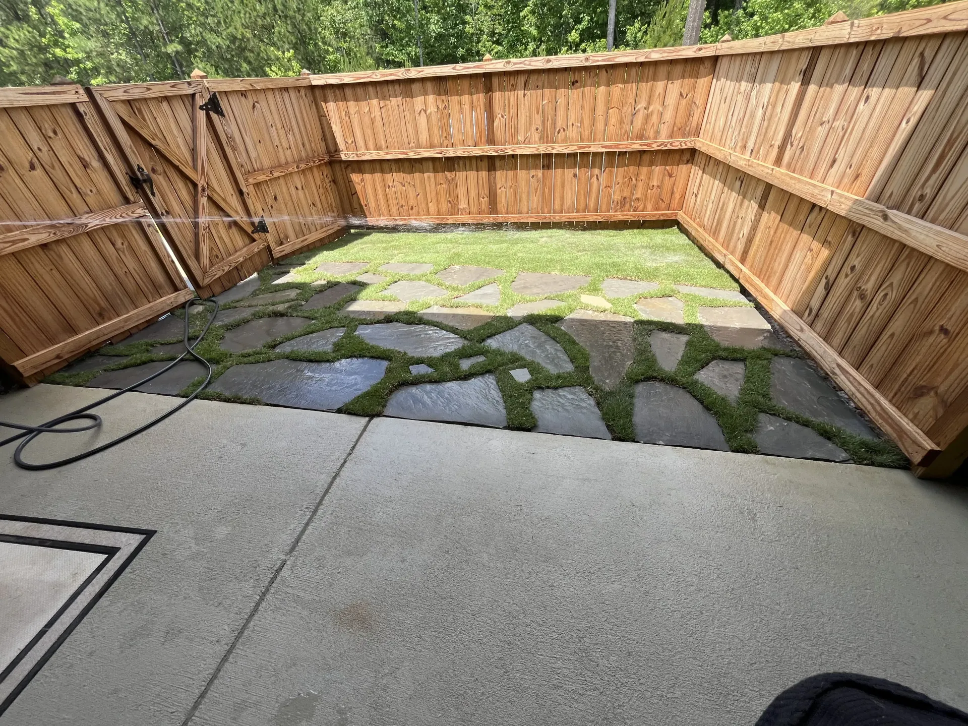 Backyard patio with stone pavers, wooden fences, and a grassy section.