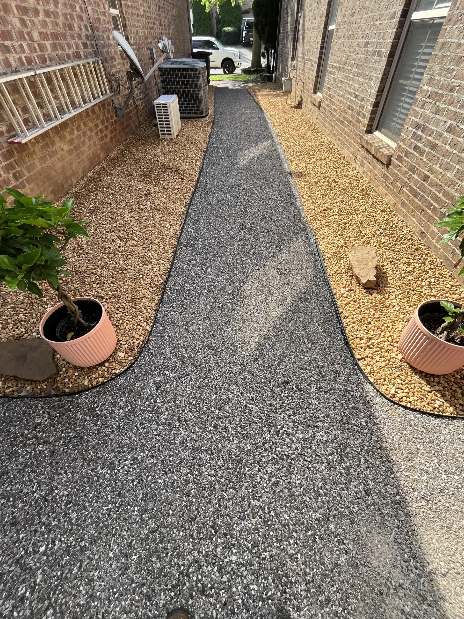 Fresh gravel path between brick walls with potted plants and mulch on both sides