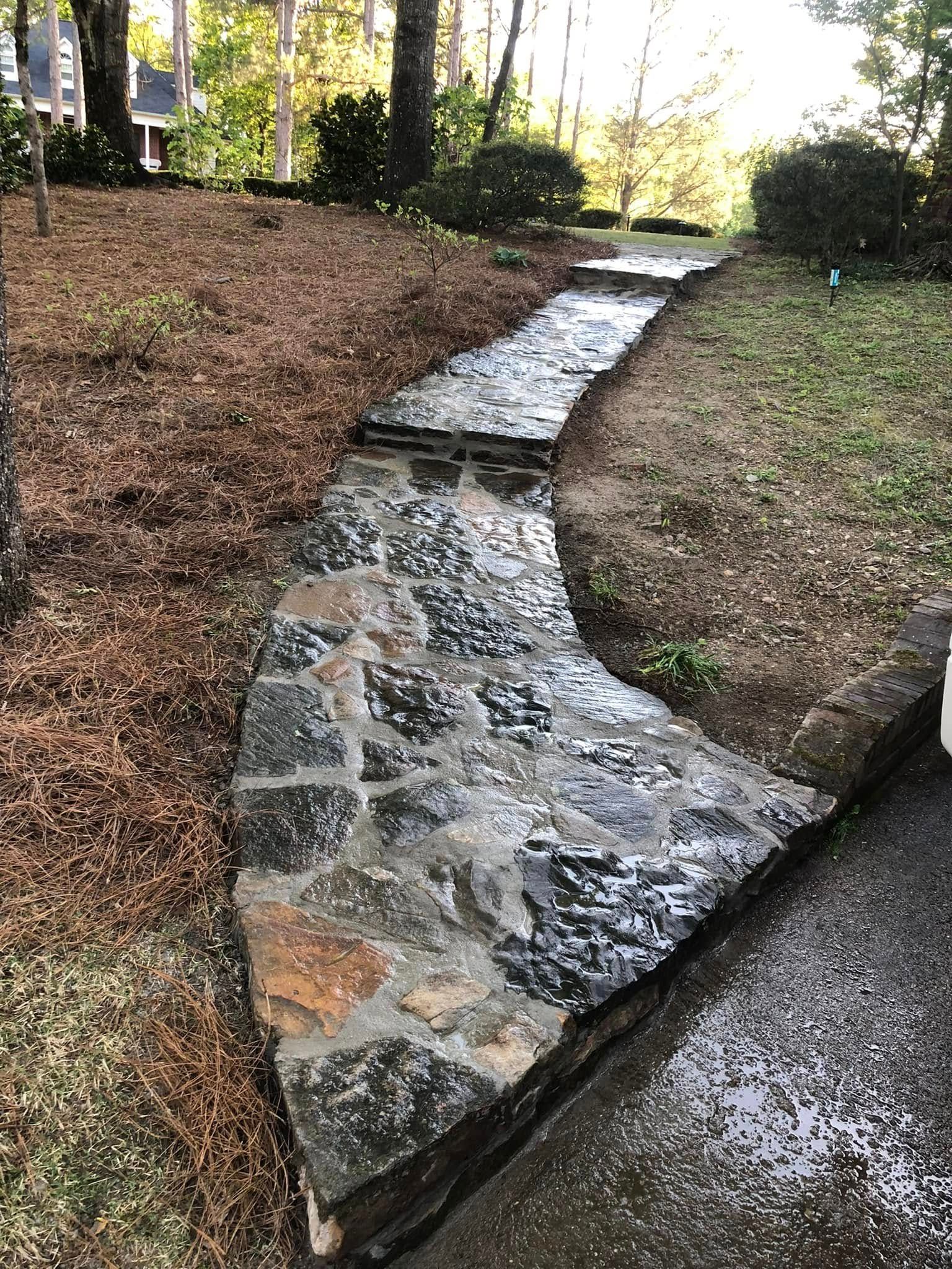 A stone walkway going through a yard next to a driveway.