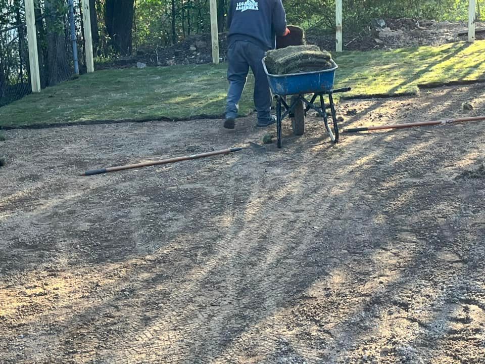 A man is pushing a wheelbarrow full of grass.