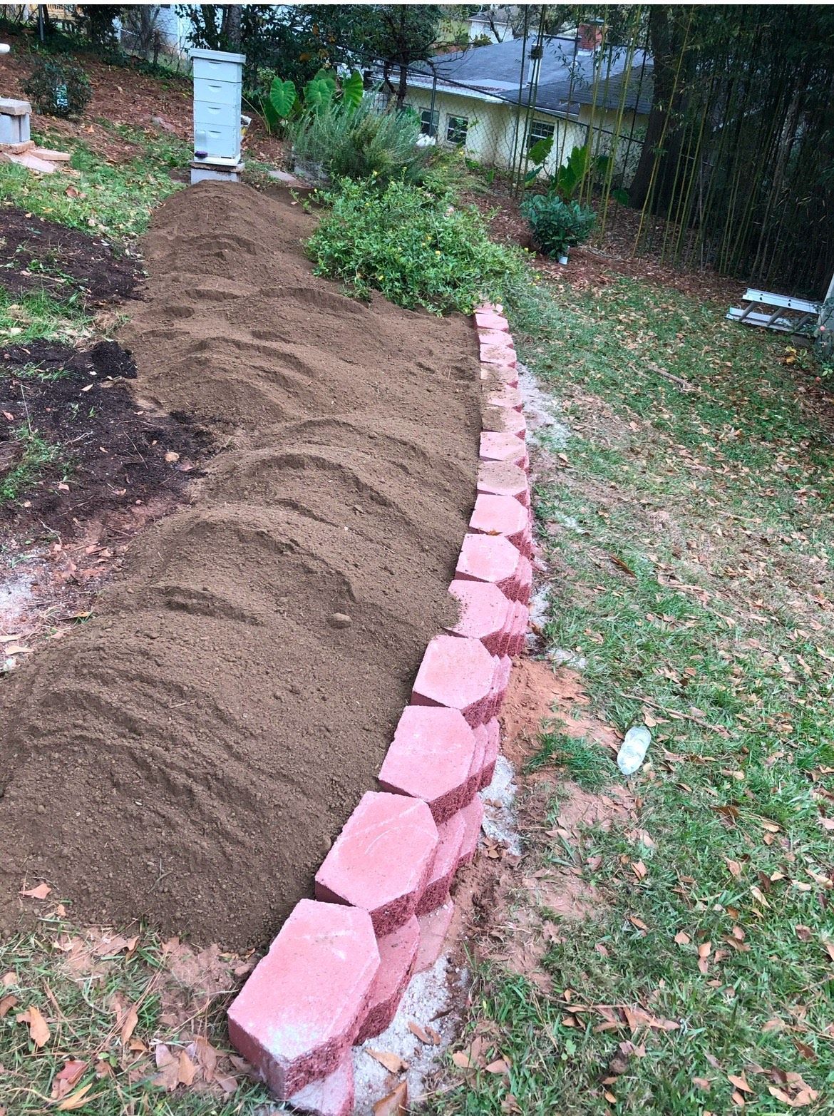 A brick wall is being built in a yard next to a pile of dirt.