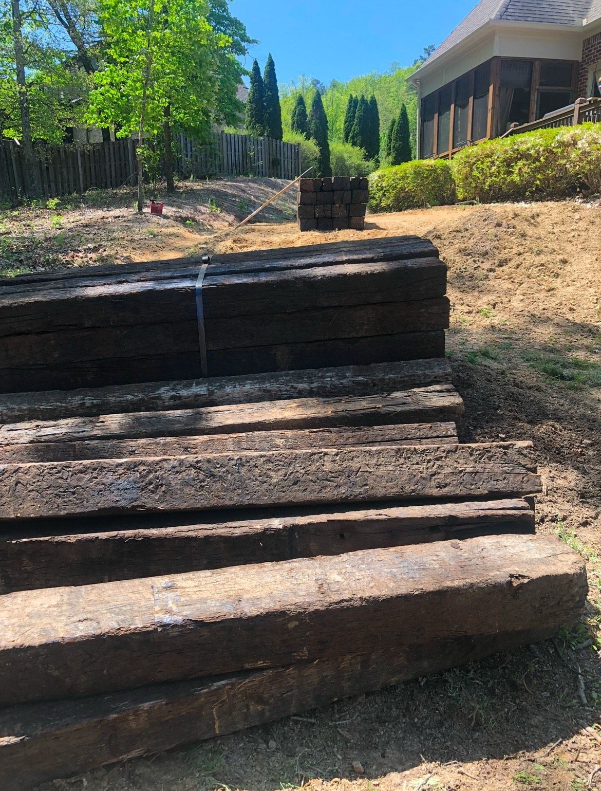 A pile of wooden beams sitting on top of a dirt hill in front of a house.