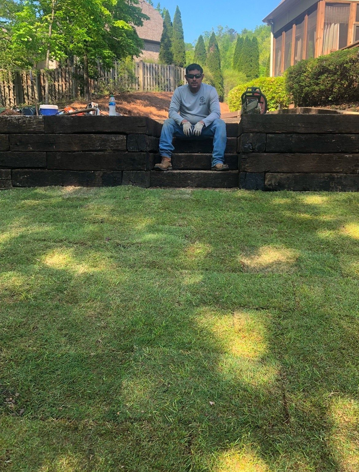 A man is sitting on a wooden wall in the grass.