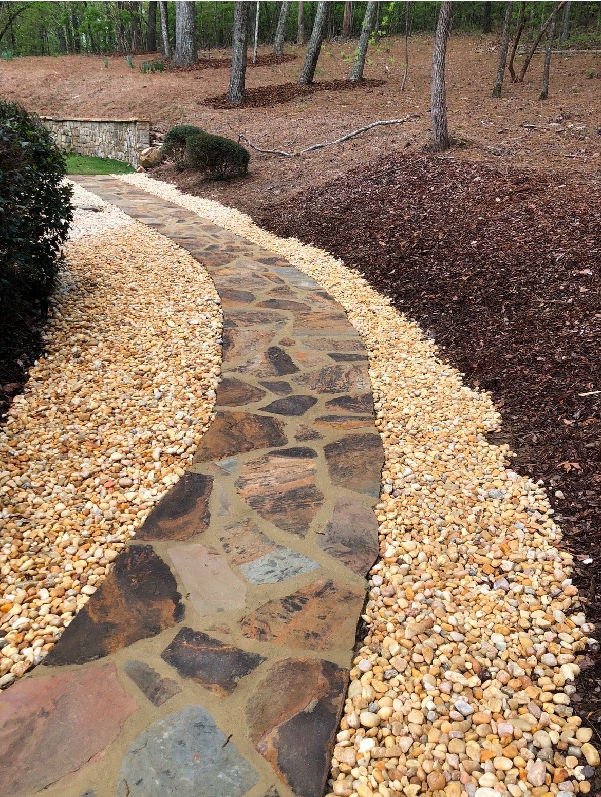 A stone walkway is surrounded by gravel and trees.