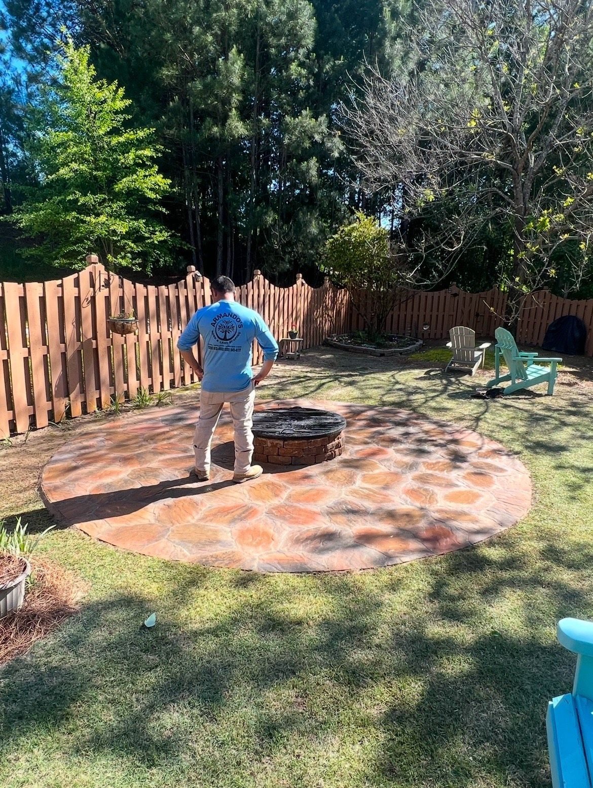 A man is standing in a backyard next to a fire pit.