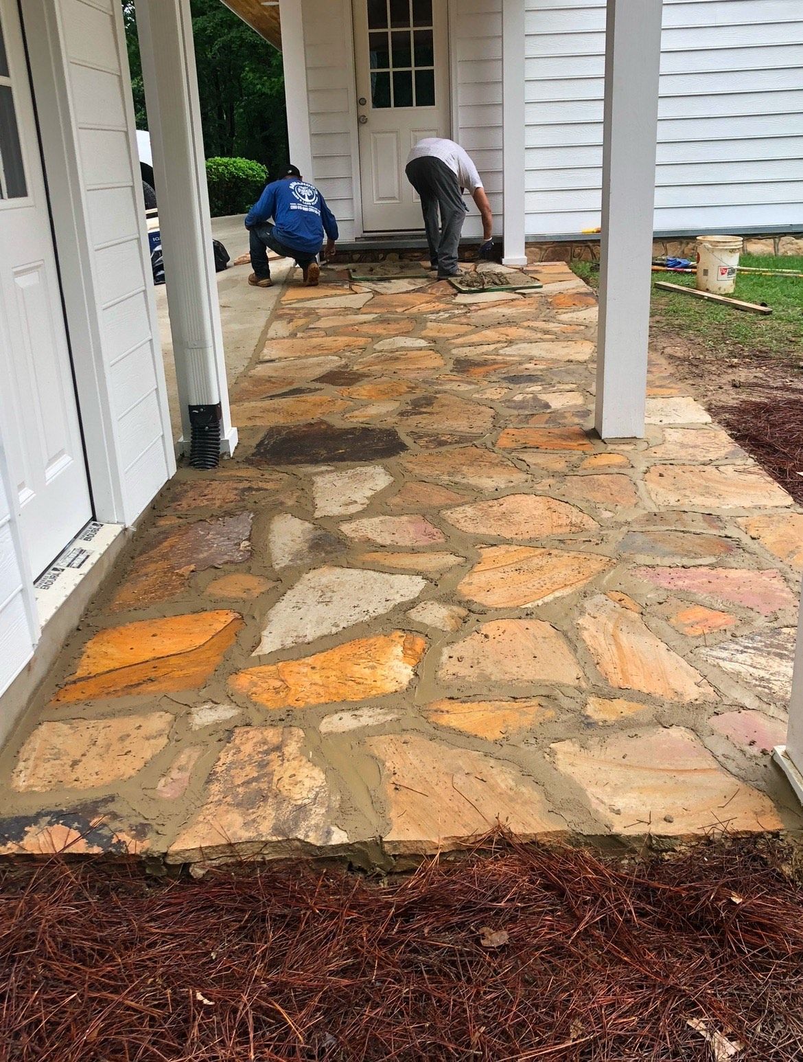 Two men are working on a stone walkway in front of a house.