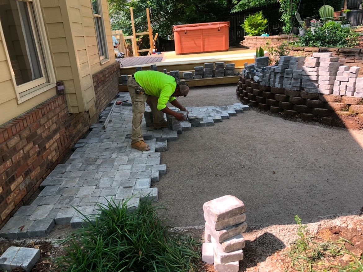 A man is laying bricks on a sidewalk in front of a house.