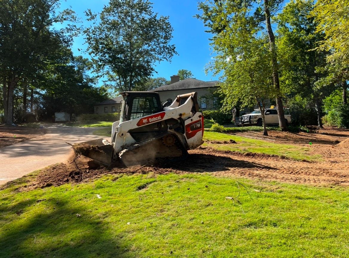 A bulldozer is digging a hole in the grass in a yard.