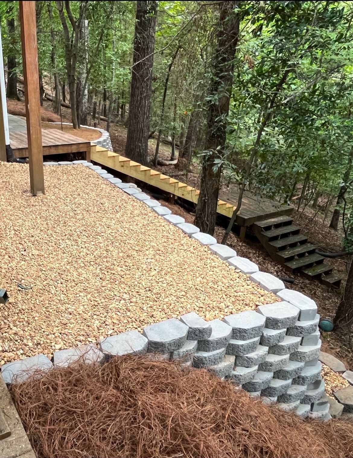 A patio with a stone wall and stairs in the woods.