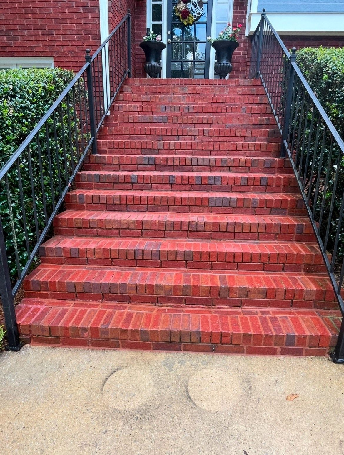 A set of red brick stairs leading up to a house with a wrought iron railing.