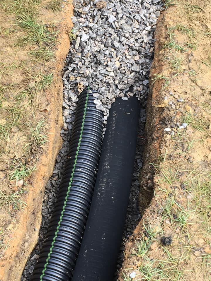A black pipe is laying in the dirt next to gravel.