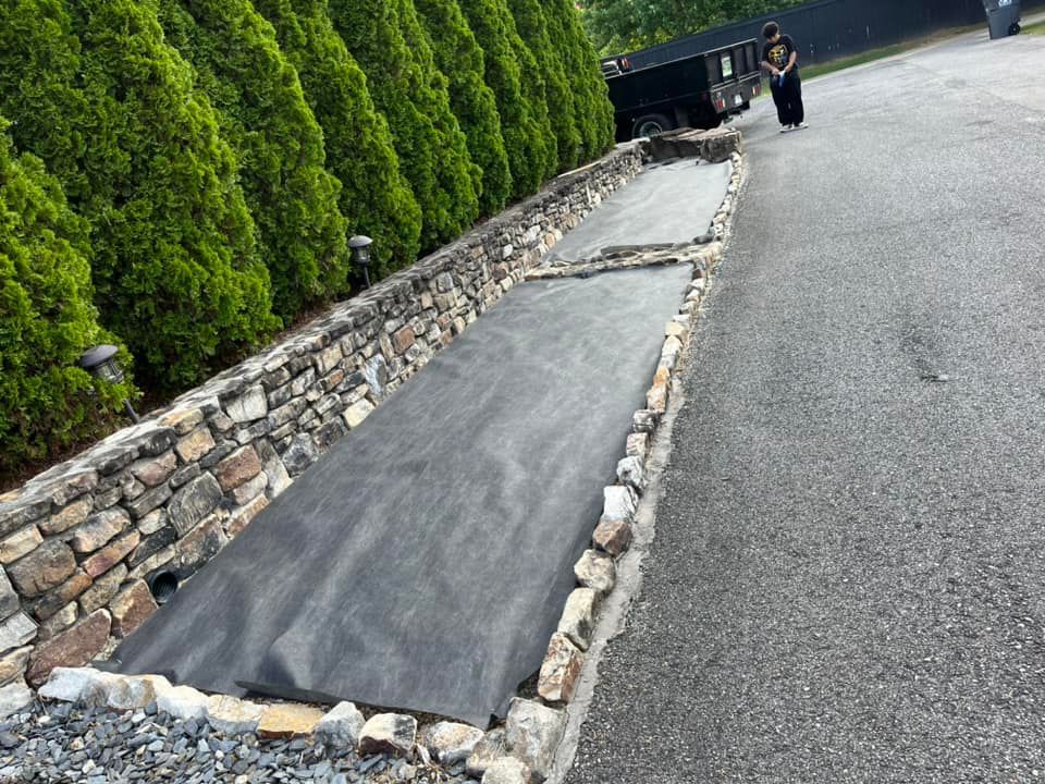 A man is standing in a driveway next to a stone wall.