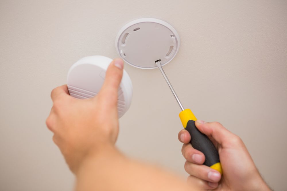 Person Installs a Smoke Detector on a White Ceiling With a Screwdriver — NTR Electrical In Toogoom, QLD