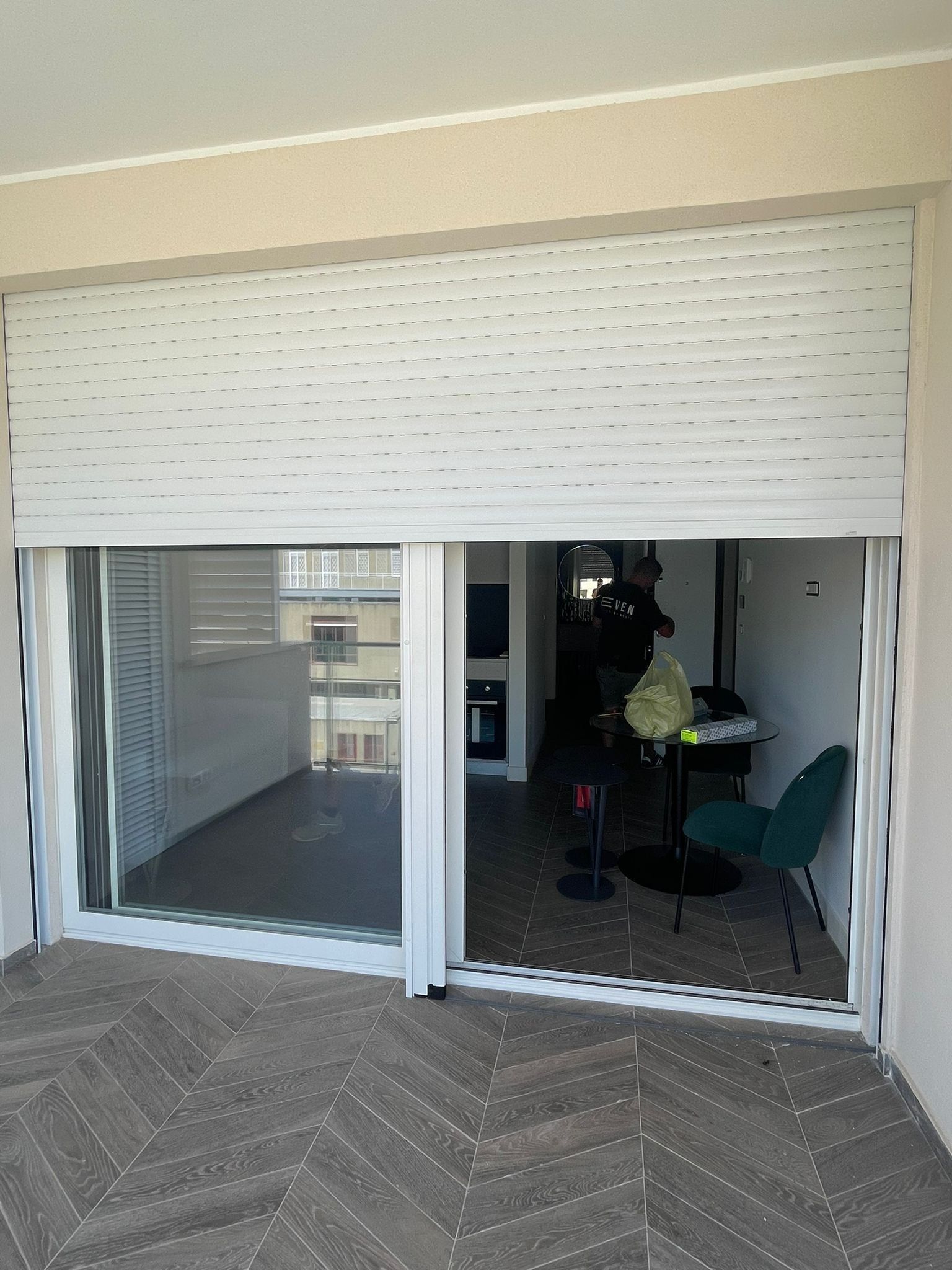 Tapparelle bianche che coprono parzialmente una porta scorrevole in vetro su un balcone.