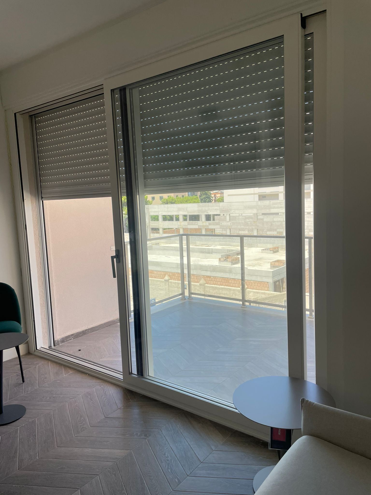 Porte scorrevoli in vetro con tapparelle chiuse, grigie e perforate, che si affacciano su un balcone con ringhiere in metallo.