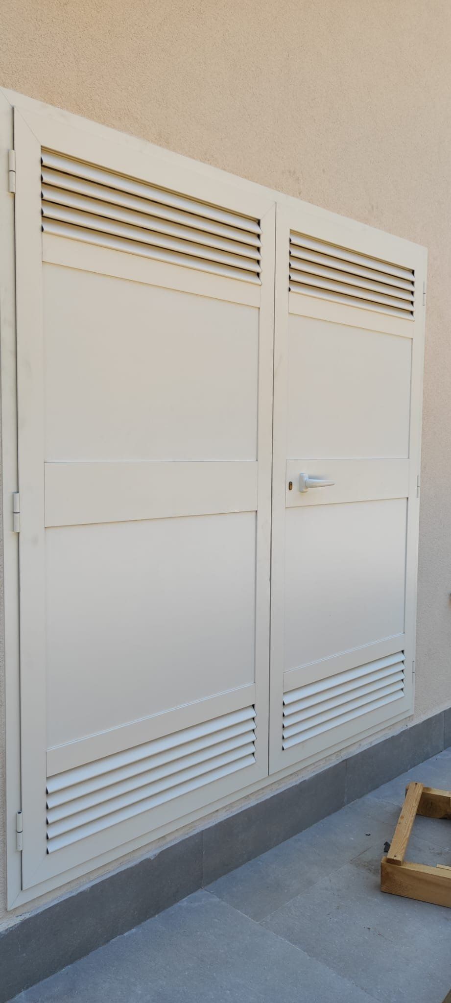 Porte in metallo bianco con feritoie orizzontali e serratura. Le porte si trovano su un edificio di colore chiaro.