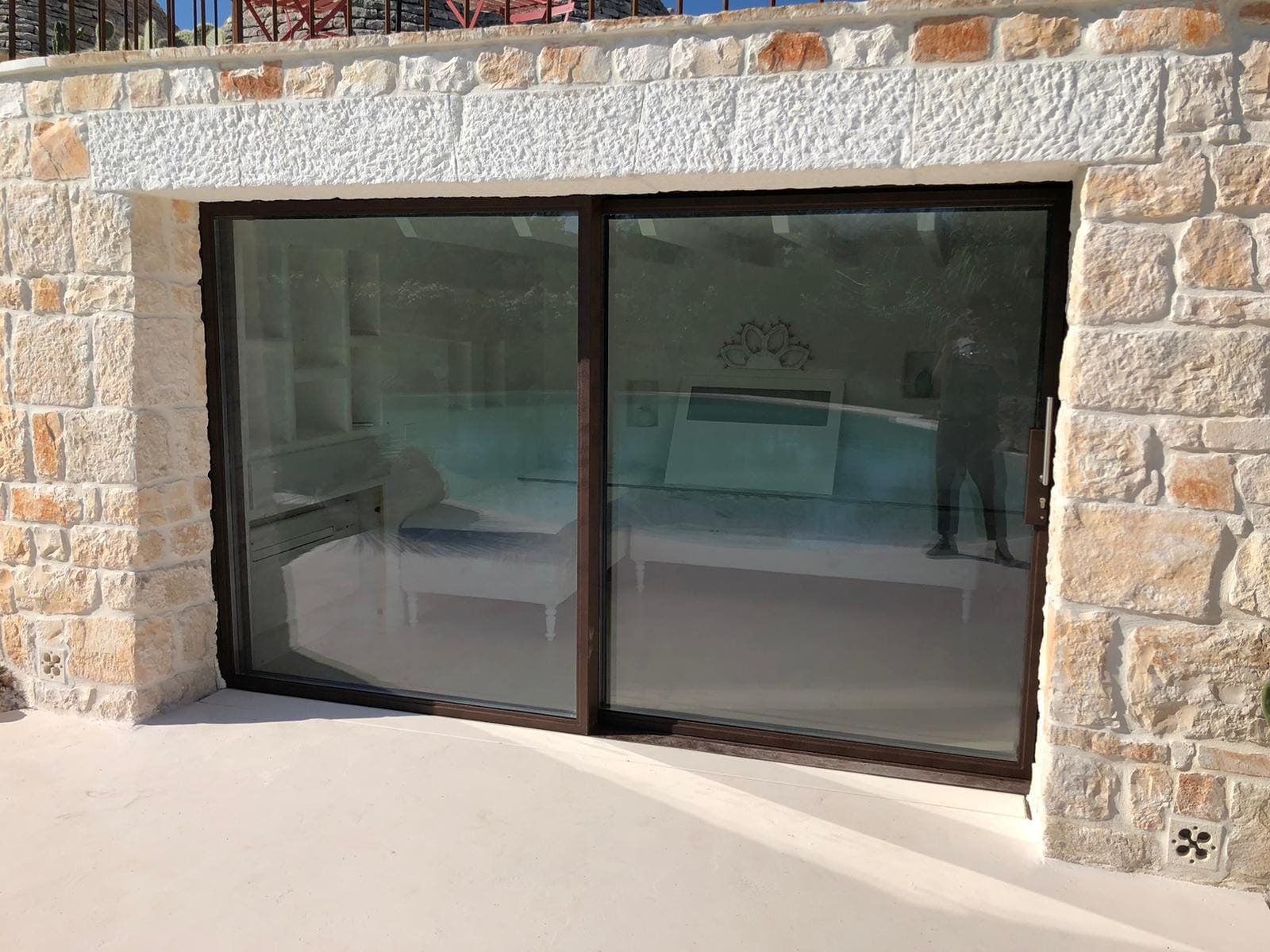 Porte scorrevoli in vetro incastonate in un muro di pietra, che riflettono una persona e l'arredamento interno.