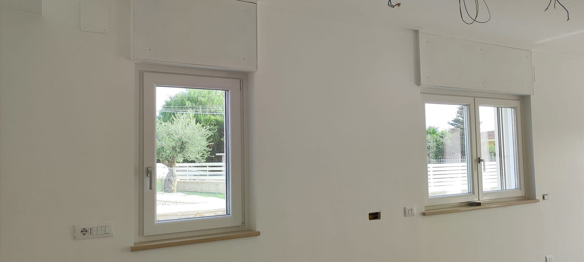 Due finestre bianche in una stanza con pareti bianche. Una finestra è aperta e rivela degli alberi.