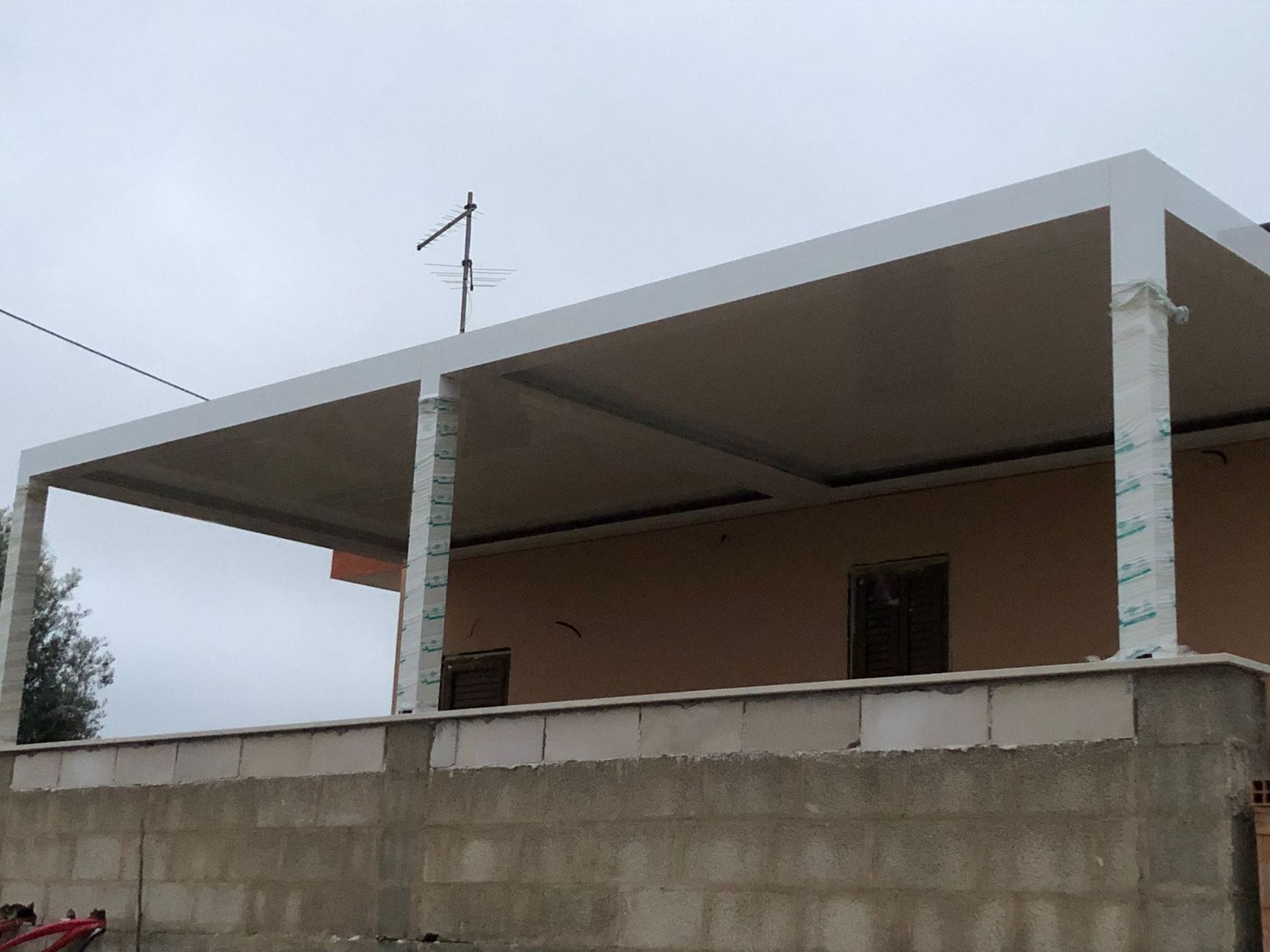 Un pergolato bianco copre l'ingresso di un edificio color sabbia. Il cielo è grigio e nuvoloso.