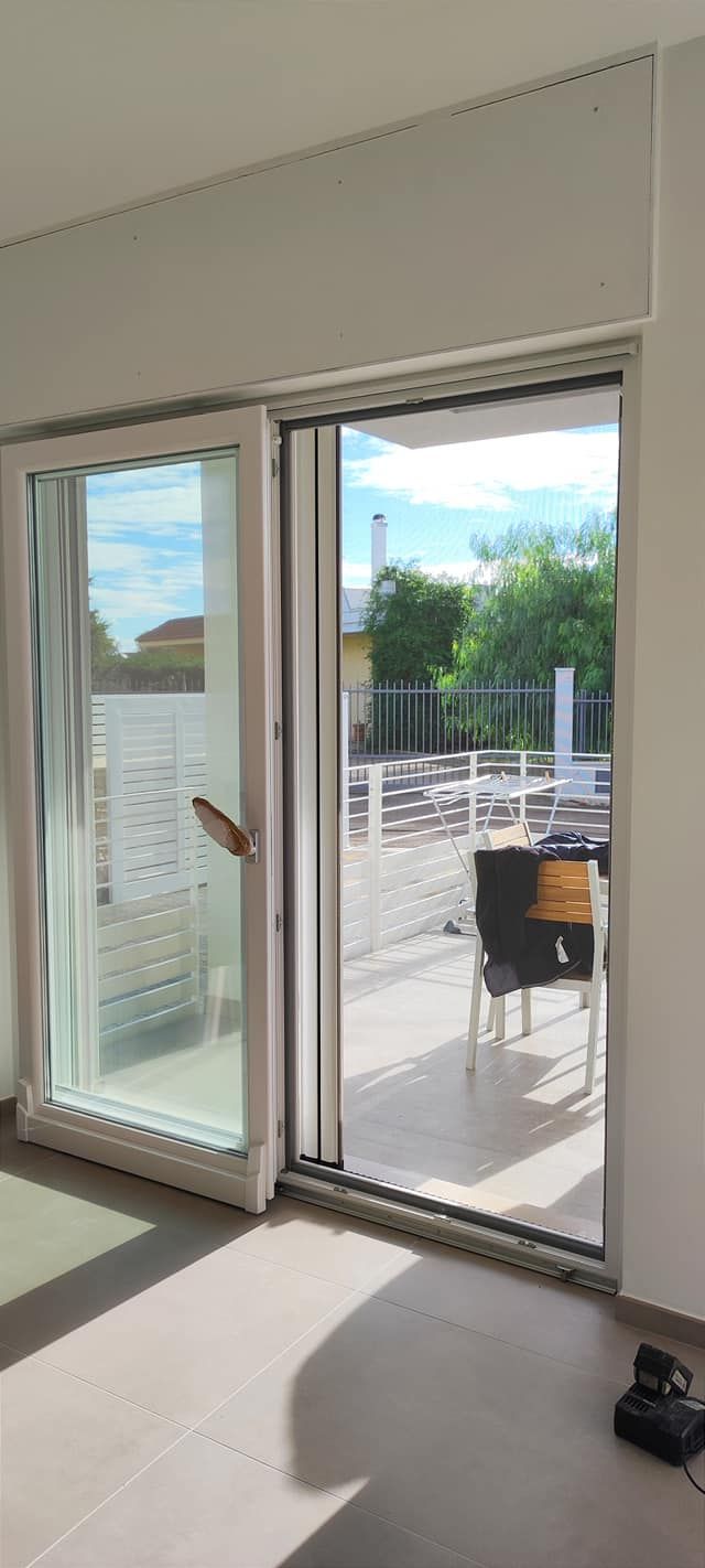 Una porta scorrevole in vetro si apre su un patio. La porta è incorniciata in bianco e offre una vista sul verde esterno.