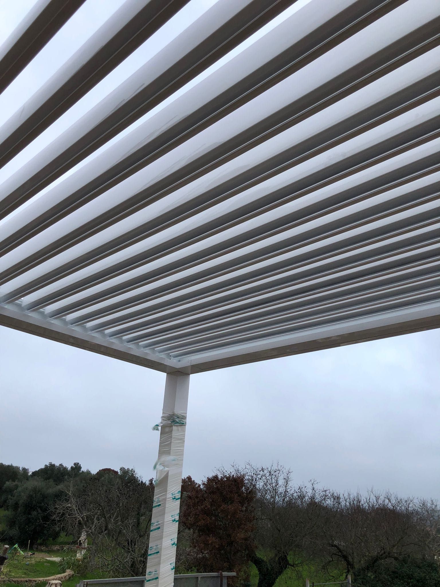 Pergola con doghe orizzontali, struttura bianca, cielo coperto, vista esterna.