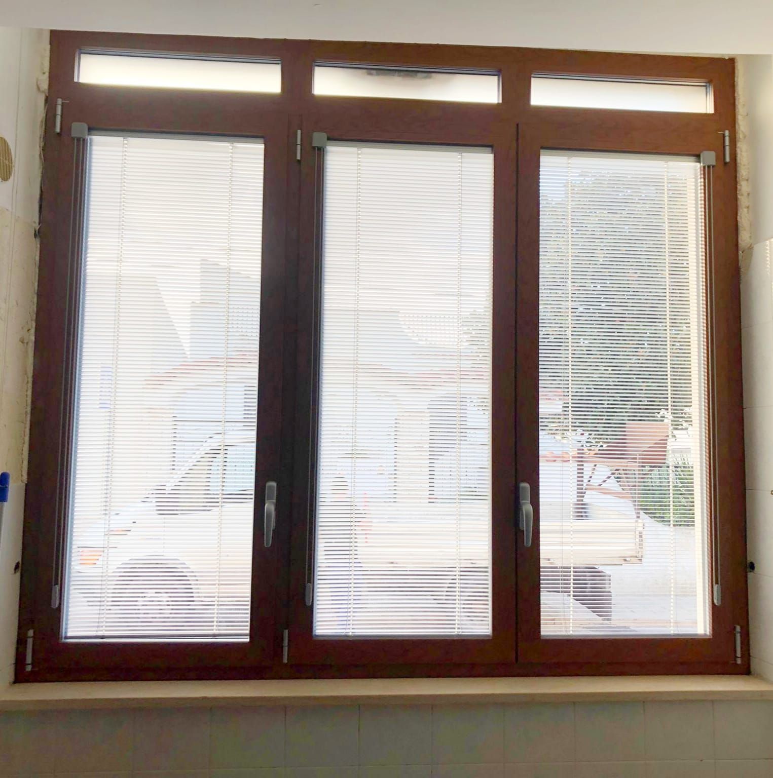 Finestra con cornice in legno e persiane, vista sull'esterno, finiture marrone chiaro.