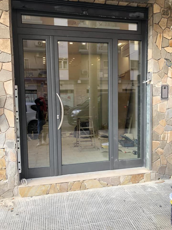 Ingresso in vetro con cornice grigio scuro e parete esterna in pietra.