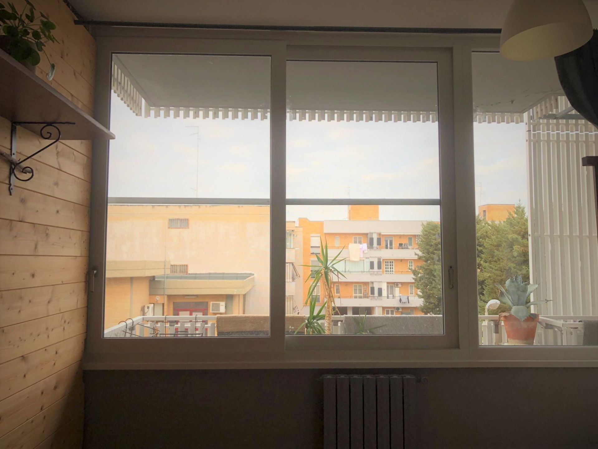 Vista dalla finestra di edifici e cielo, con un termosifone sotto la finestra.