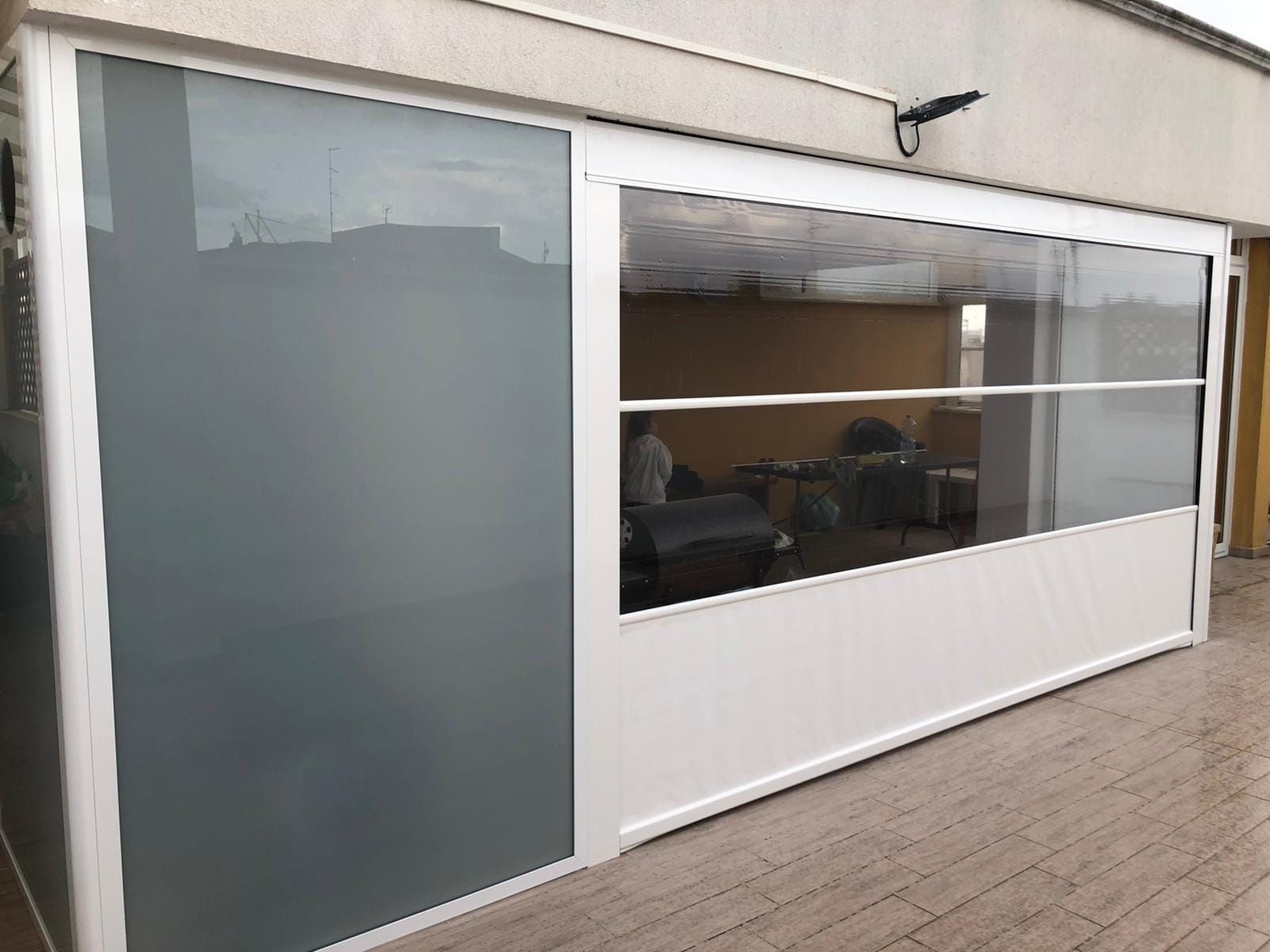 Parete in vetro con cornice bianca su un patio. Pannello in vetro smerigliato sulla sinistra. Porte scorrevoli in vetro rivelano l'arredamento interno.