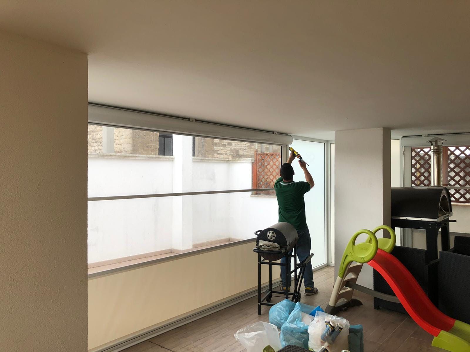 Un uomo pulisce una grande finestra con un tergivetro. È in piedi su uno sgabello.