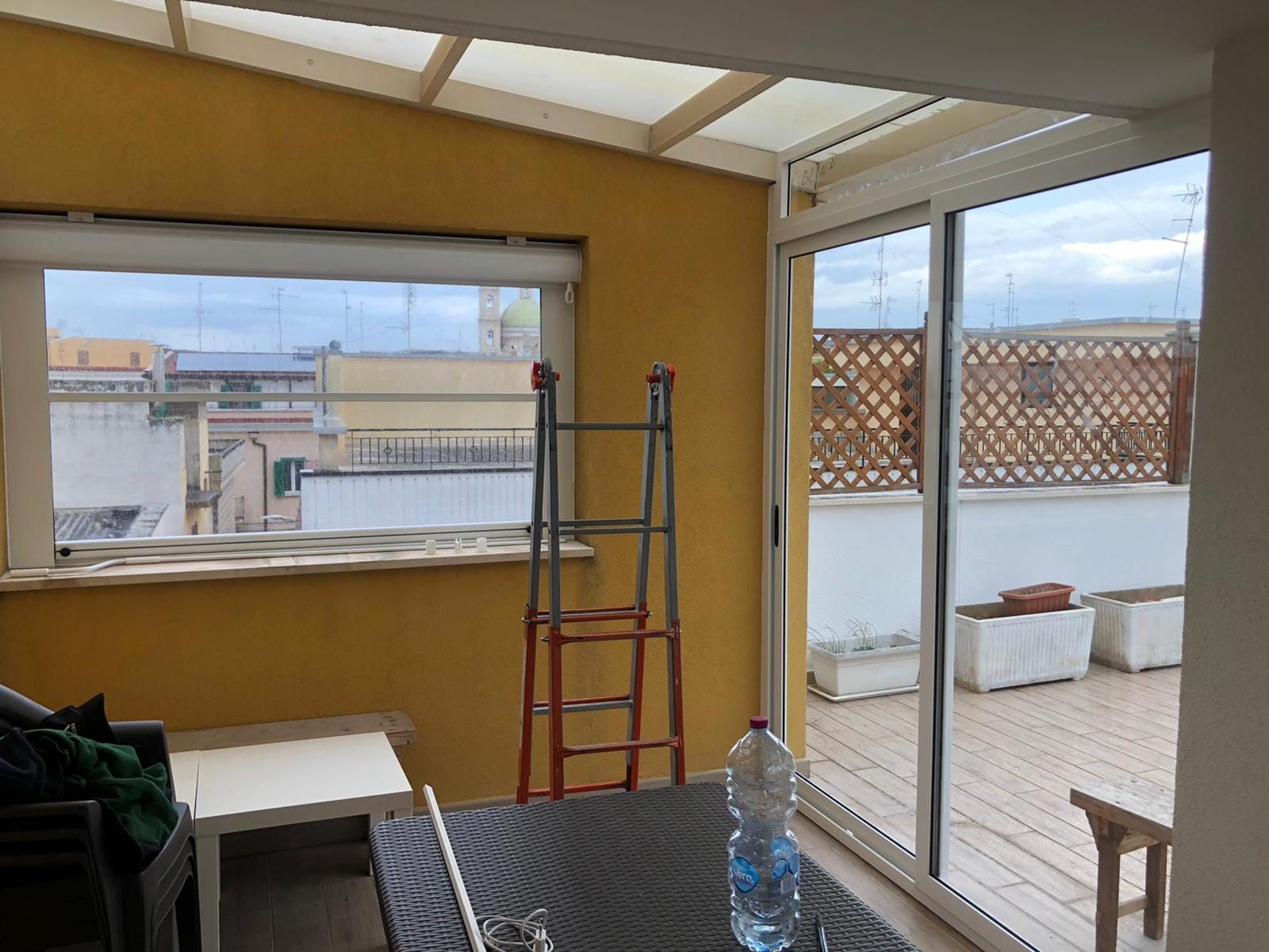 Una veranda con pareti gialle, una scala e una vista sui tetti attraverso la finestra.