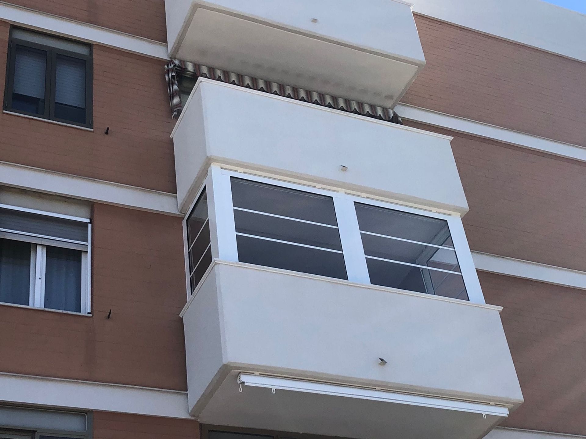 Vista esterna di un edificio con un balcone bianco, in contrasto con una facciata in mattoni marroni.