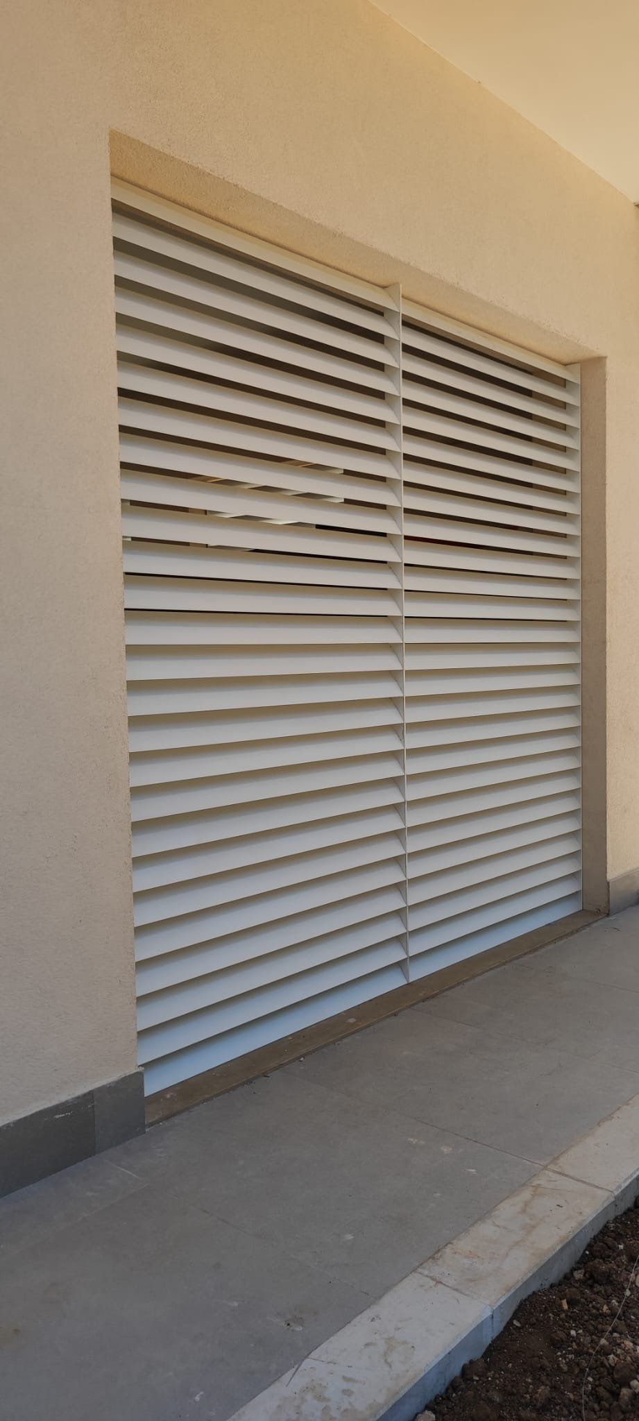 Parete esterna con persiane orizzontali bianche; in primo piano un camminamento in cemento.