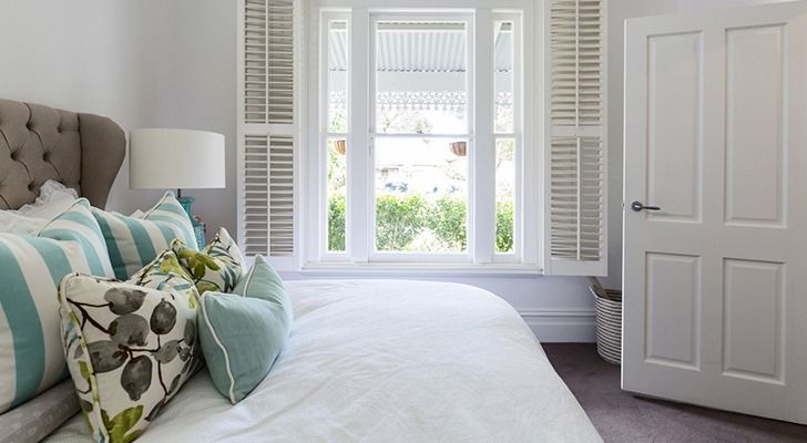 Camera da letto con letto, cuscini, finestra con persiane e porta bianca.
