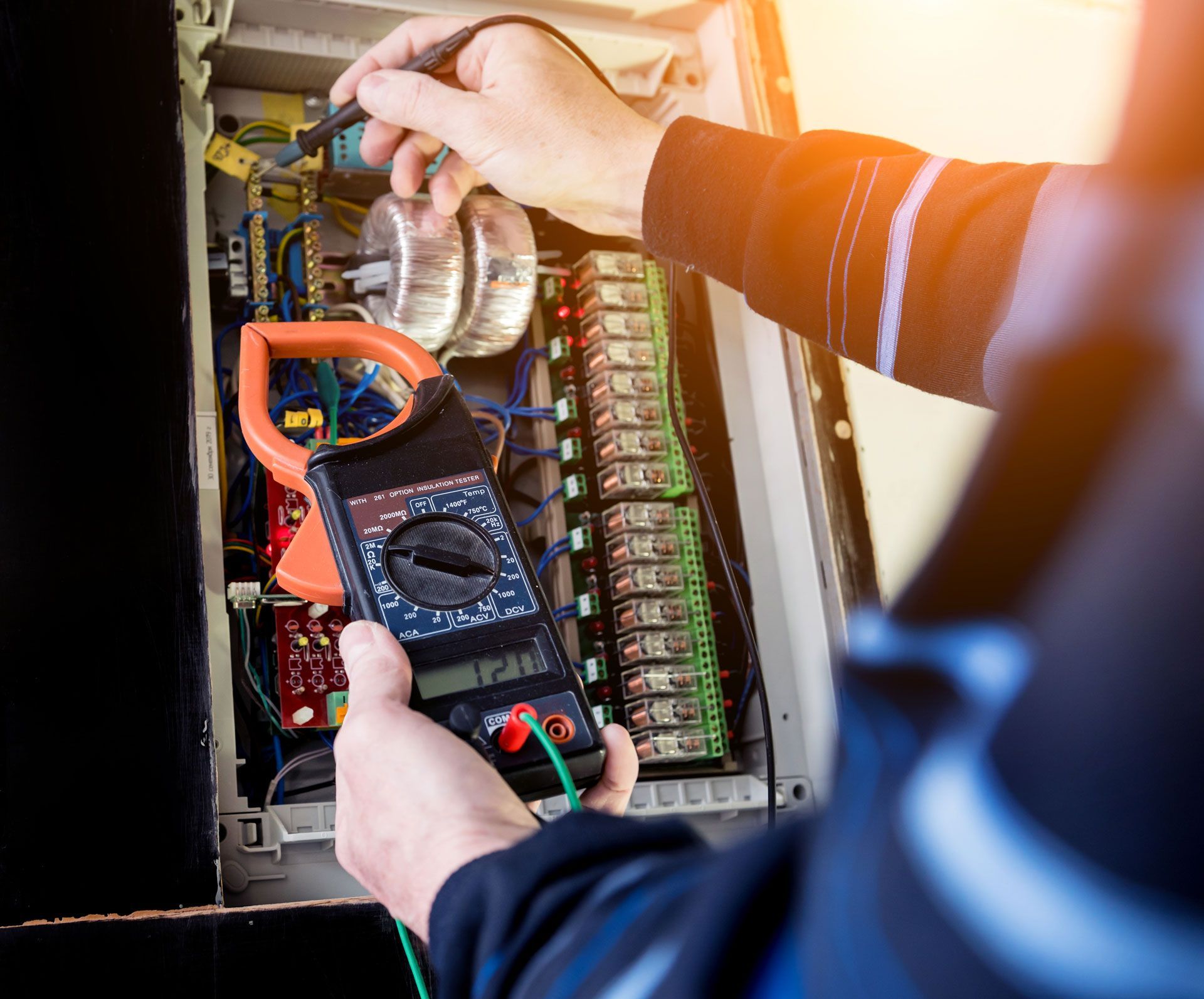 Technician testing electrical panel with multimeter and screwdriver inside an open cabinet