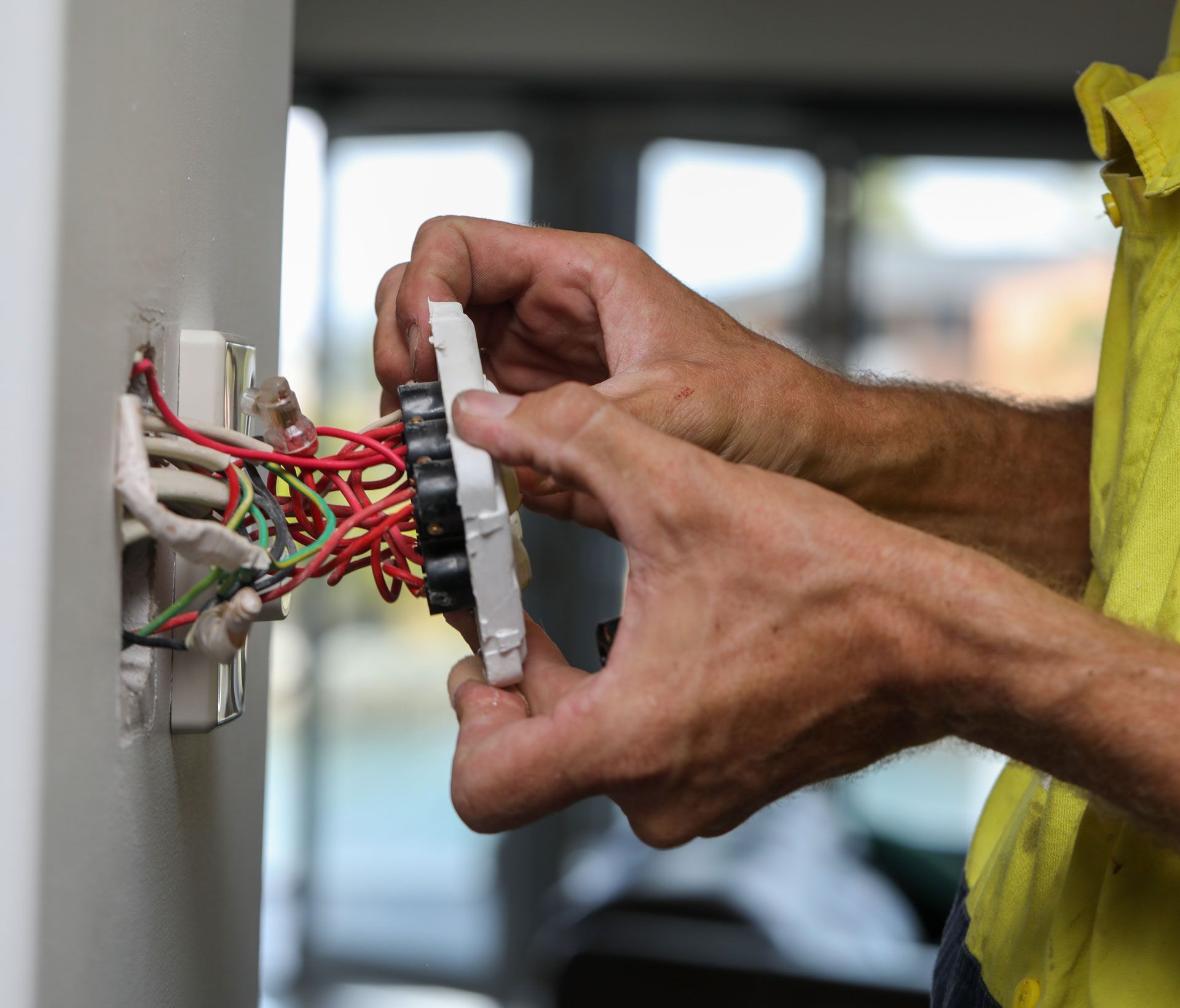 Electrician wiring a wall outlet, connecting red and white wires with a screwdriver.
