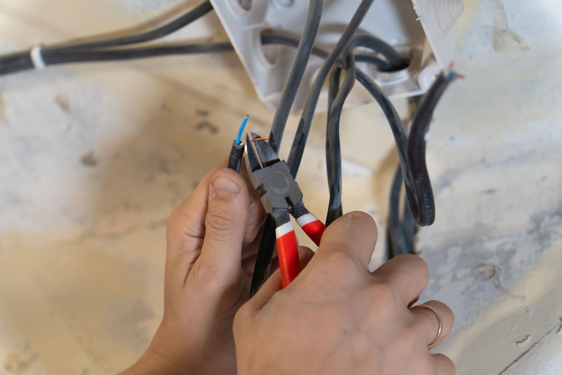 Hands using red-handled pliers to work on exposed electrical wires and cables.