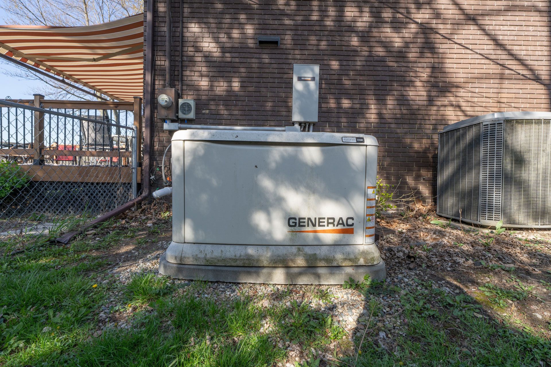 Outdoor Generac backup generator beside a brick house, with a small utility shed nearby