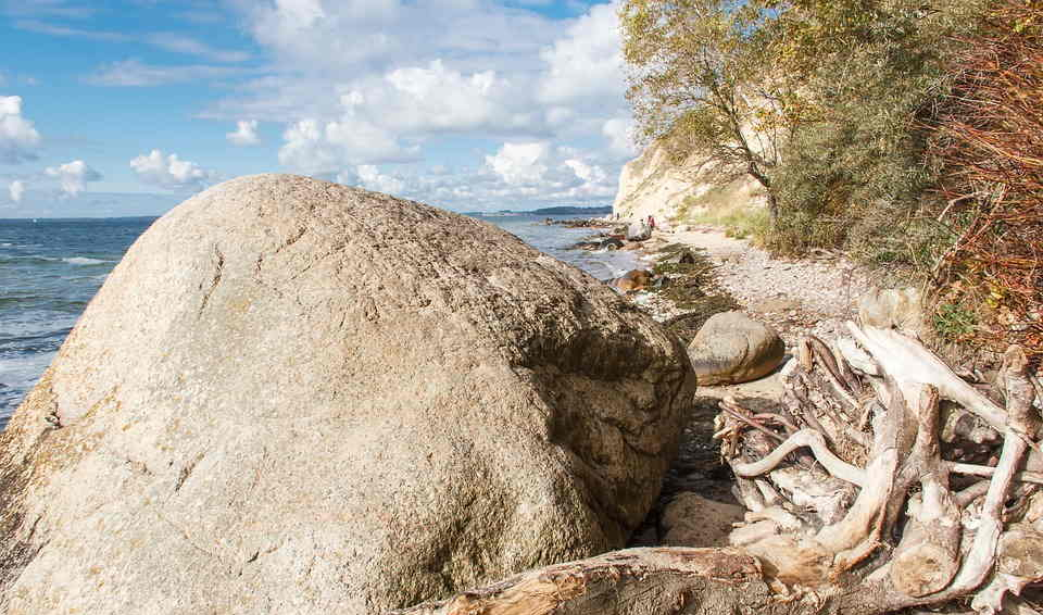 Ein großer Felsen liegt an einem Strand neben dem Meer.