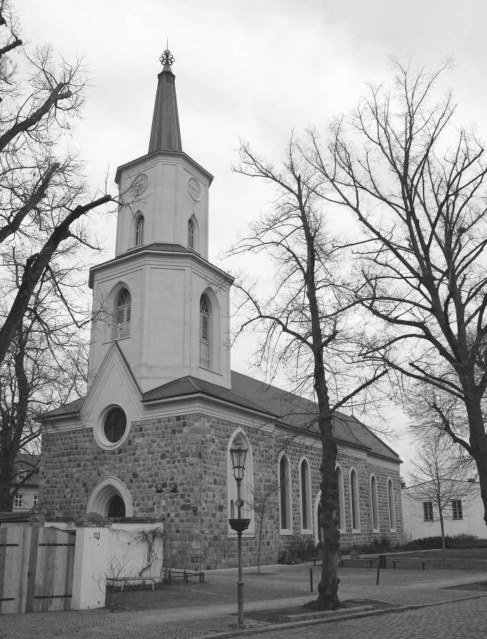 Ein Schwarzweißfoto einer Kirche mit einem Glockenturm, umgeben von Bäumen.
