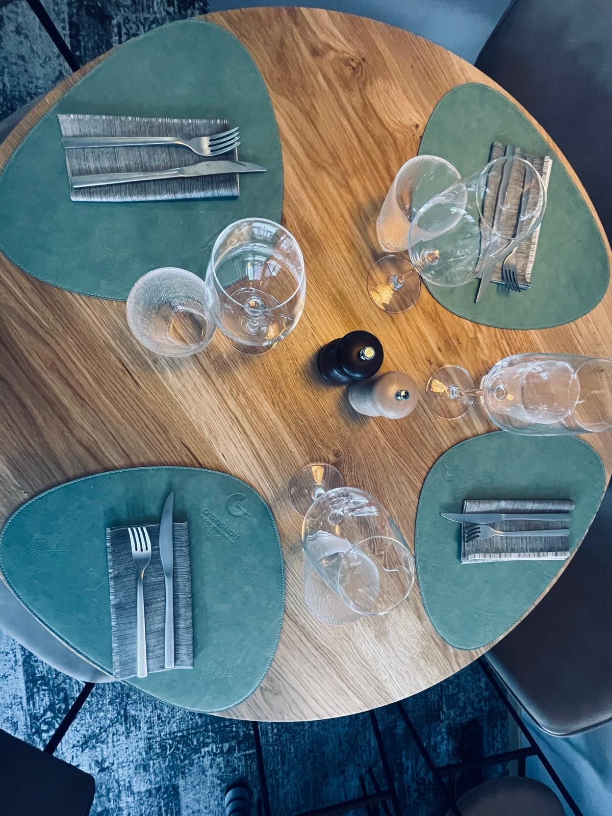 Une table en bois avec des sets de table verts et des ustensiles dessus.