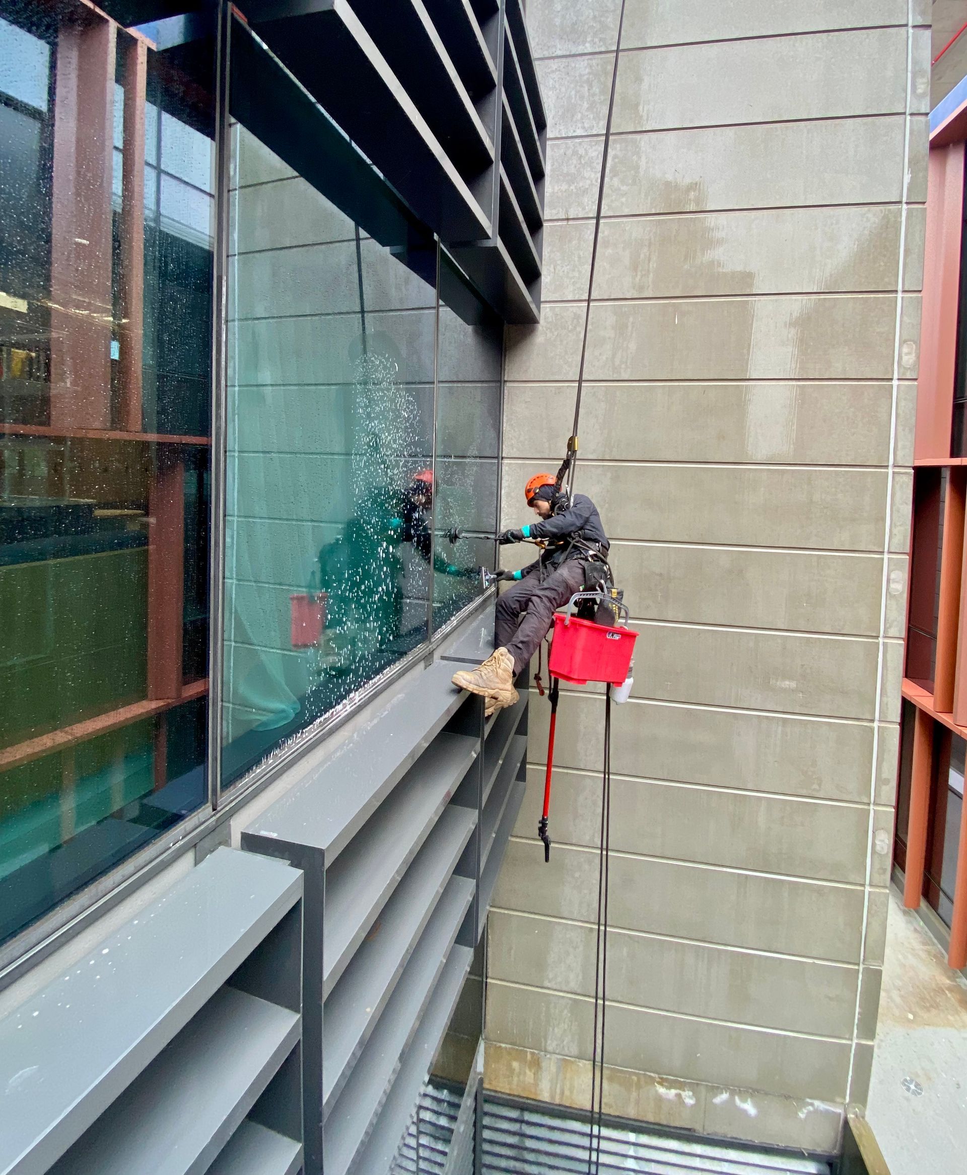A Man cleaning windowns outside a high rise building — Freshwater Exterior Cleaning in Lennox Head, NSW
