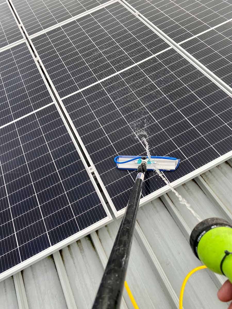 A Person Is Cleaning Solar Panels With A Hose — Freshwater Exterior Cleaning in Lennox Head, NSW